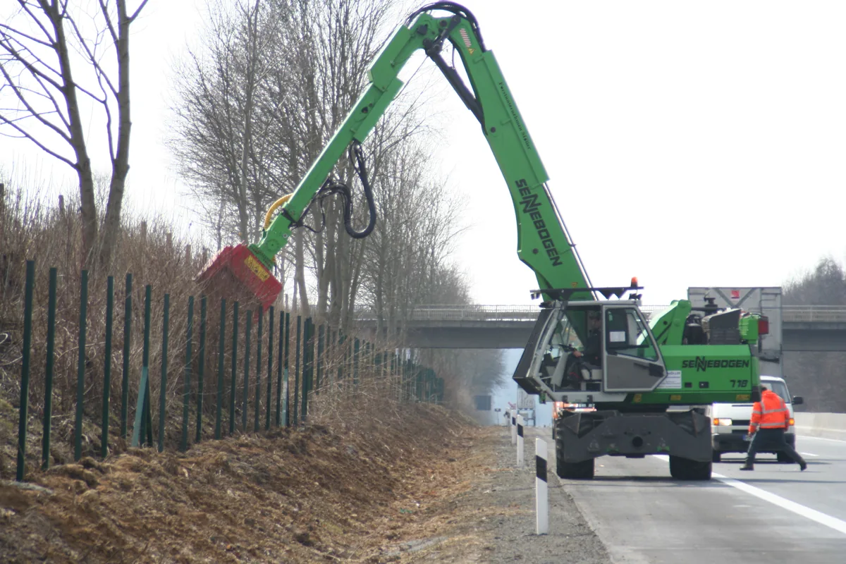 Excavator-mounted forestry mulcher cutting brush along a fence line
